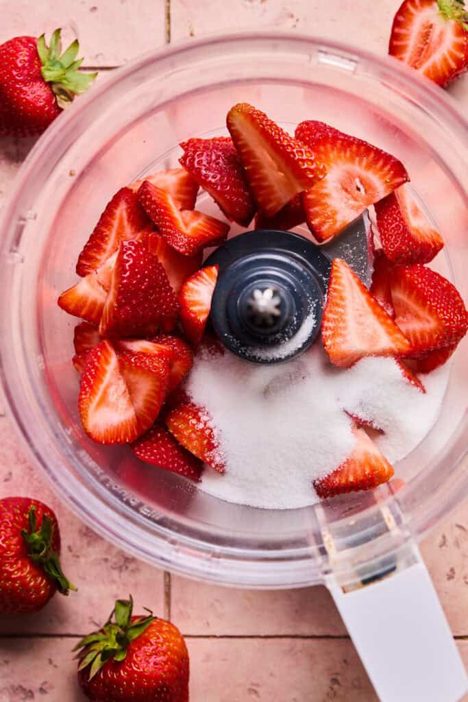 Strawberries and sugar in a food processor bowl.