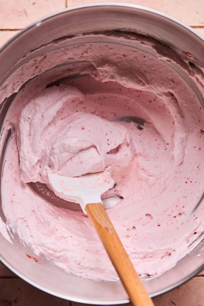 Strawberry puree and whipping cream being folded with a spatula.