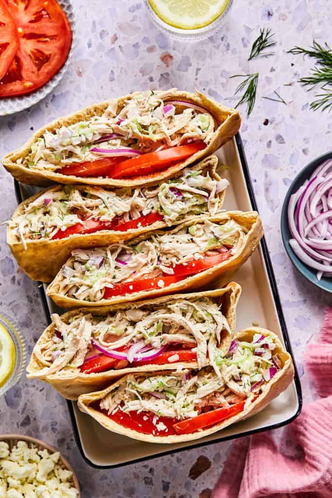 Tzatziki Chicken Salad in pitas with tomato and red onion on a tray.