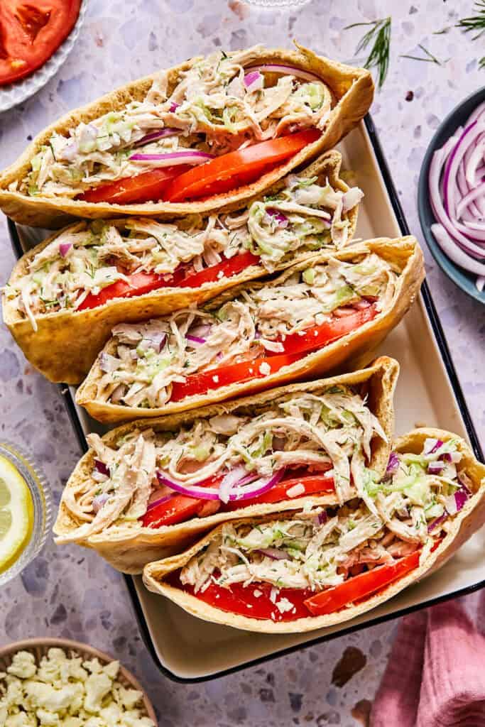 Tzatziki Chicken Salad in pitas with tomato and red onion on a tray.