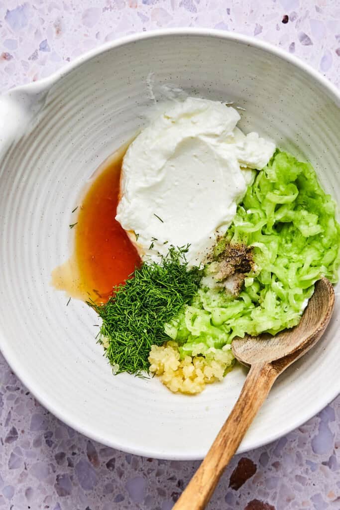 Ingredients for Tzatziki Chicken Salad in a bowl with a wooden spoon before being mixed together.
