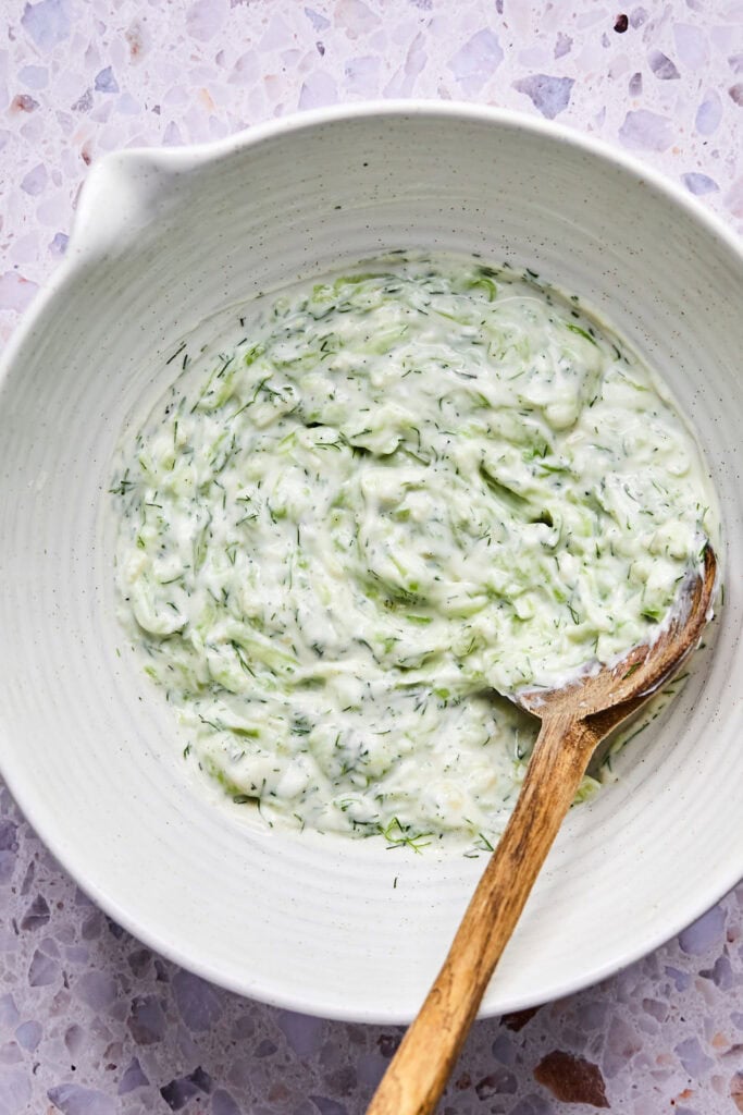 Ingredients for Tzatziki Chicken Salad mixed other in a bowl with a wooden spoon.