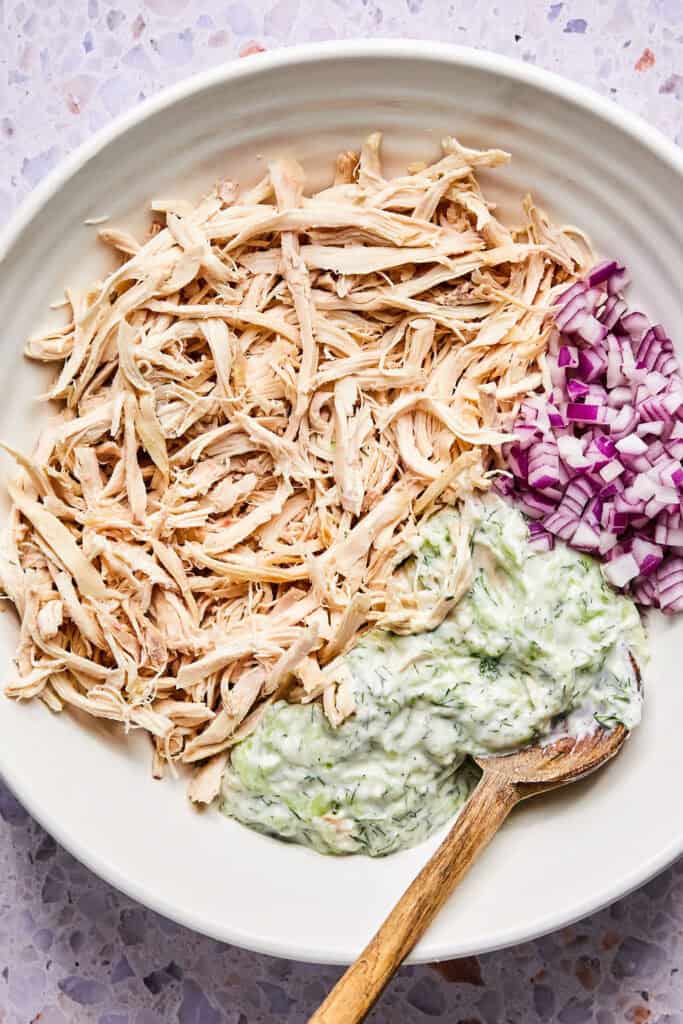 Cooked chicken and red onion added to the mixture in a bowl with a wooden spoon.