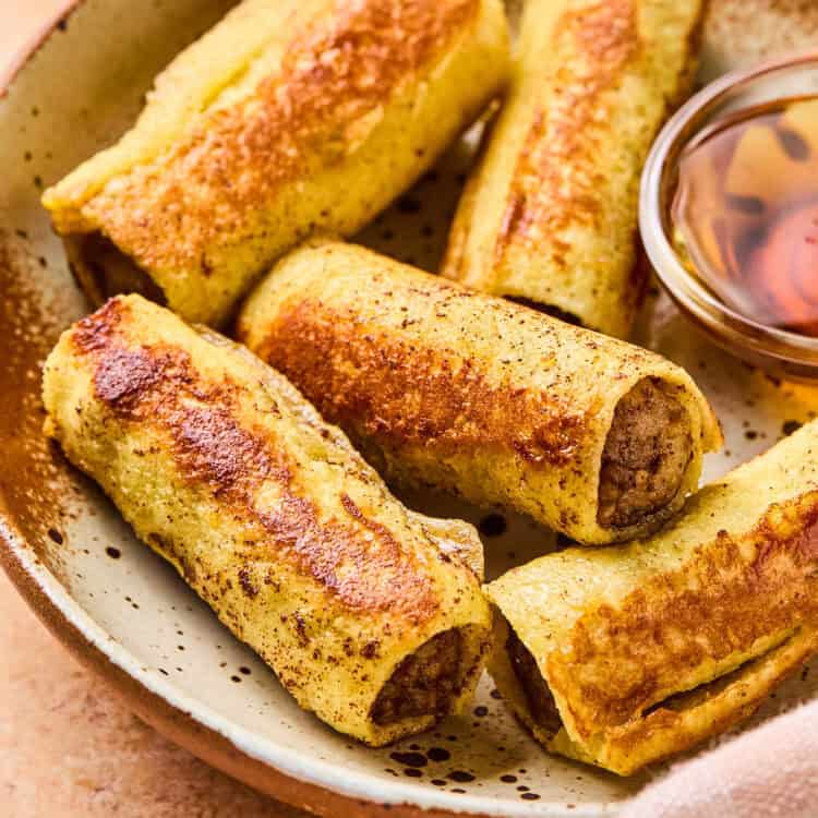 Sausage French Toast Roll ups on a plate with a side of syrup.