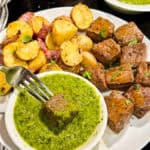 Chimichurri Steak Bites with red potatoes and a side of chimichurri sauce on a plate with a fork.