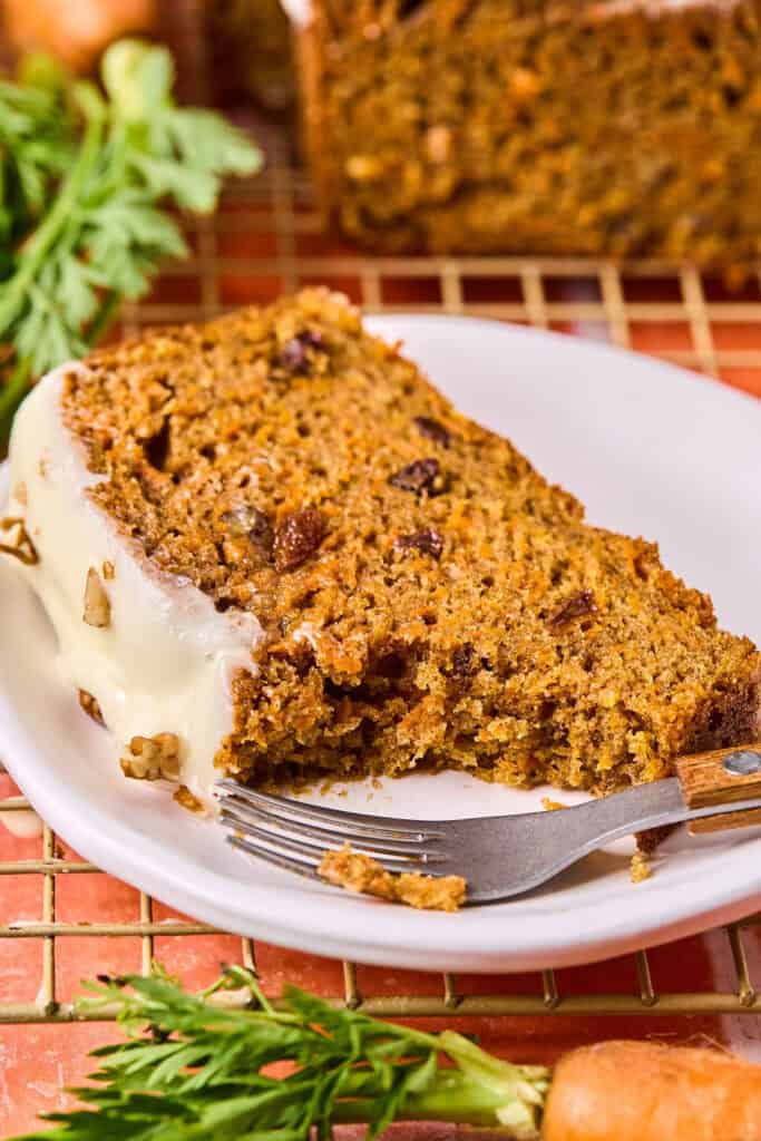 A slice of carrot cake loaf on a small plate with a fork.