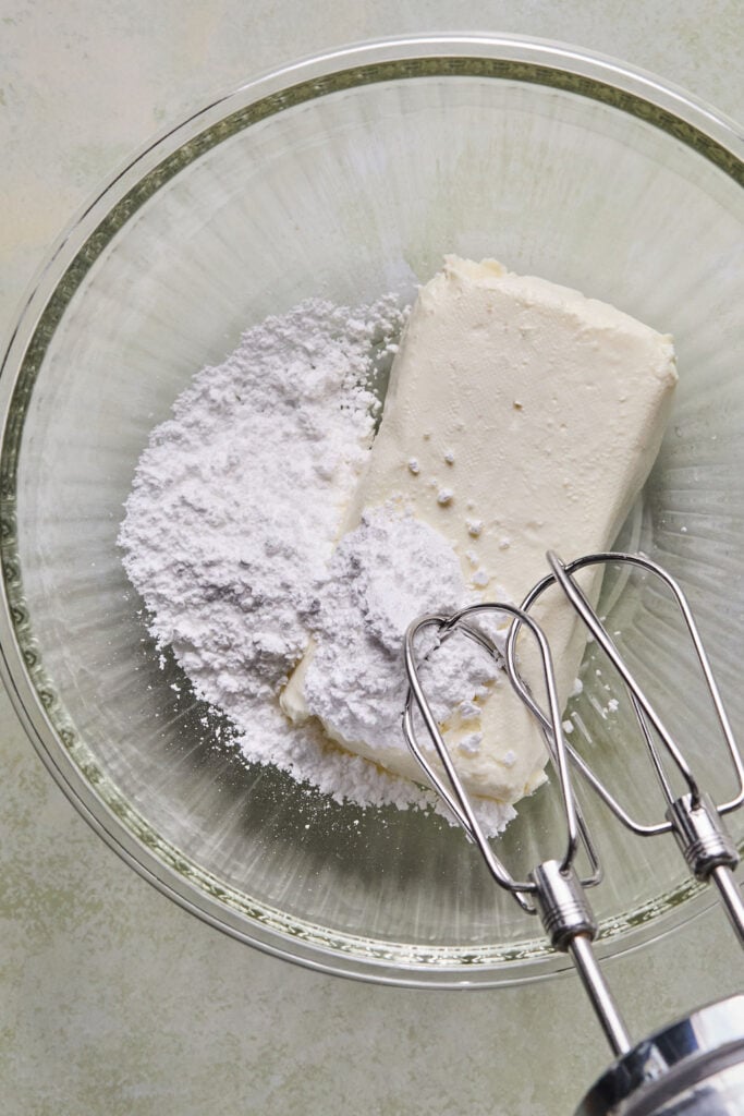Cream cheese and powdered sugar in a mixing bowl with an electric mixer.