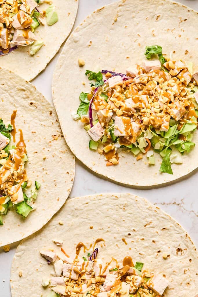 Peanut sauce being drizzled on top of the Peanut chicken crunch wrap ingredients in the tortillas.