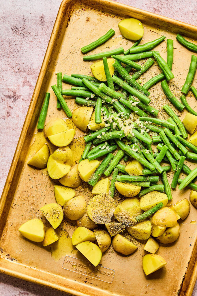 Green beans and quartered potatoes on a baking sheet.