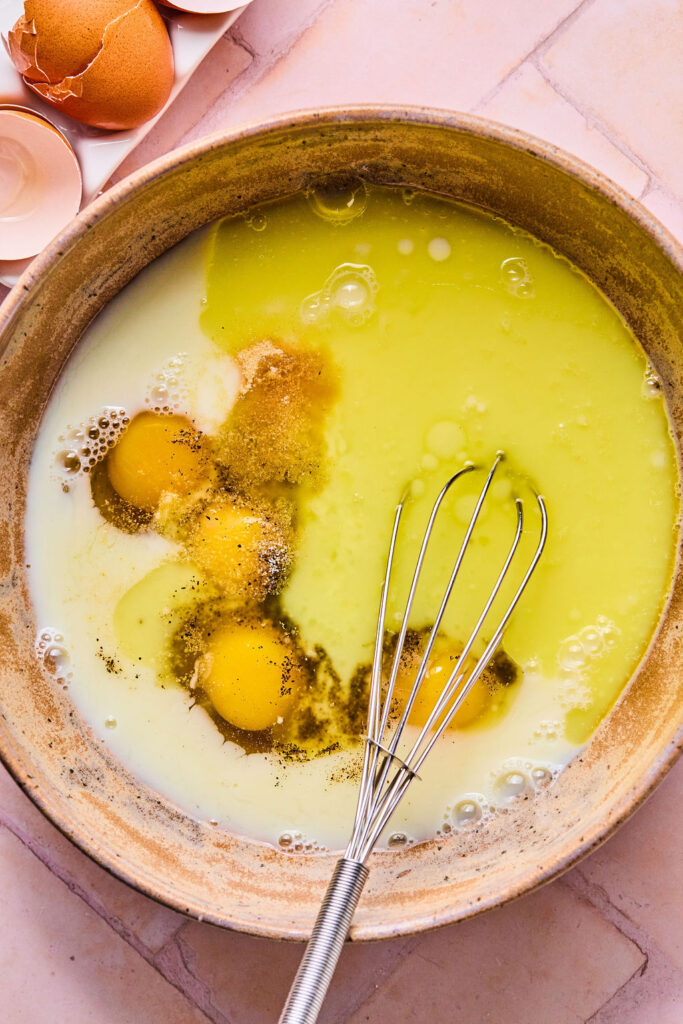Eggs, butter, and seasonings in a bowl with a whisk.