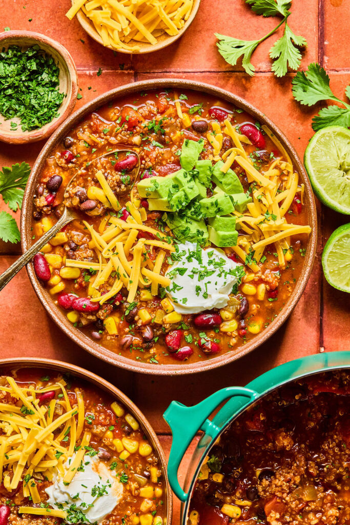 High Fiber Quinoa Chili in bowls topped with shredded cheese, avocado, and sour cream.