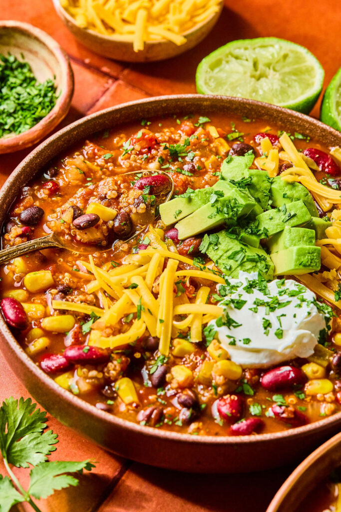 High Fiber Quinoa Chili in a bowl topped with shredded cheese, avocado, and sour cream.