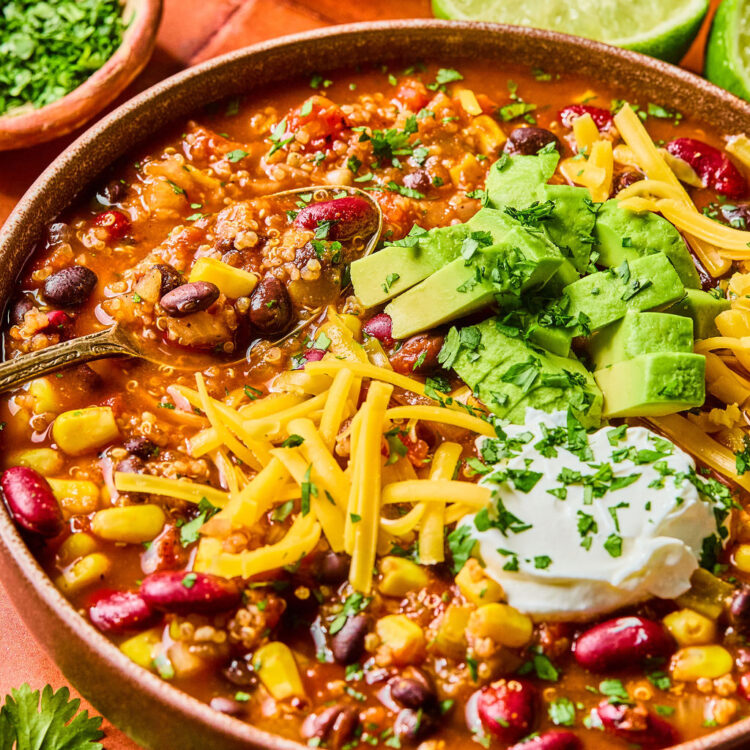 High Fiber Quinoa Chili in a bowl topped with shredded cheese, avocado, and sour cream.