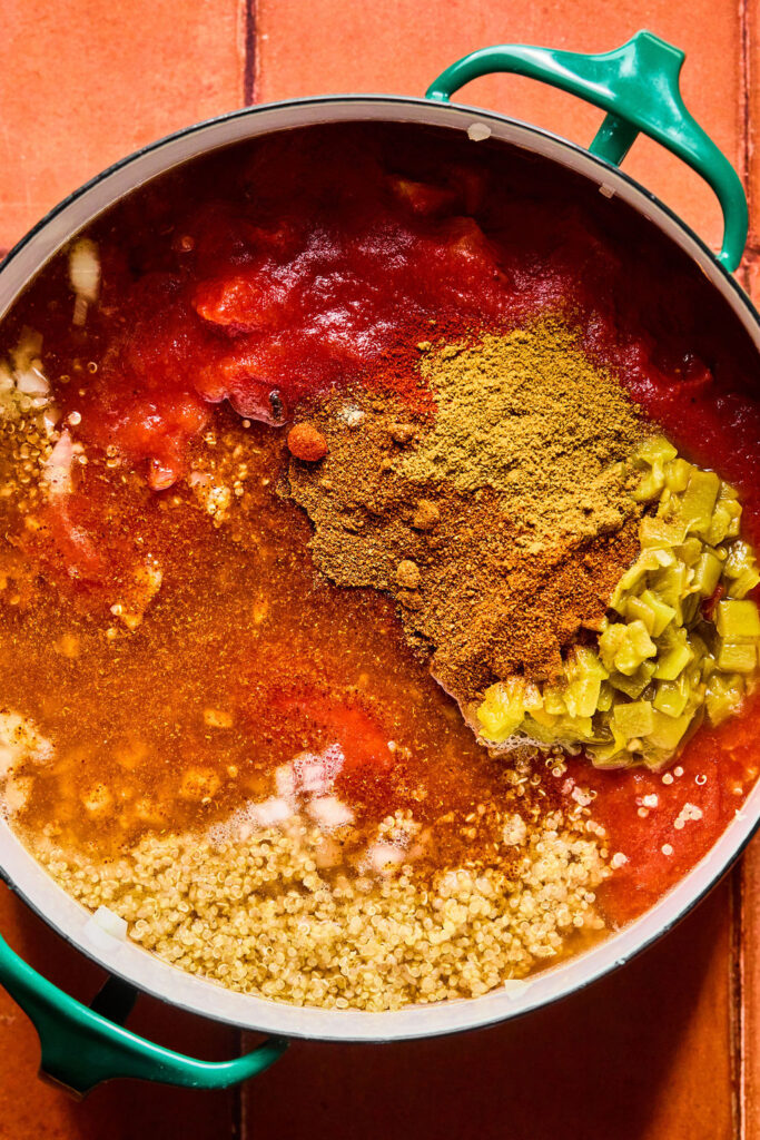 Cooked quinoa, diced tomatoes, tomato sauce, chili powder, cumin, and paprika being added to the pot.
