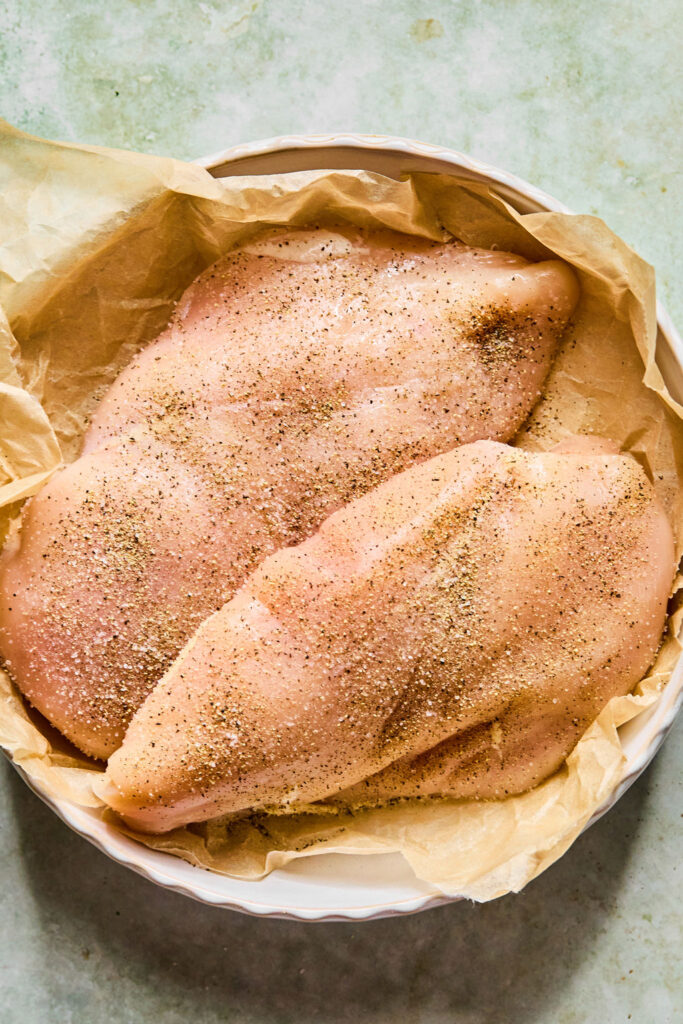 Seasoned raw chicken breasts in a bowl with parchment paper.
