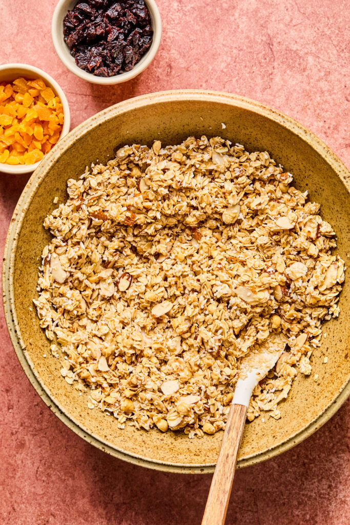 Ingredients for Hazelnut Maple Granola in a mixing bowl with a spoon.