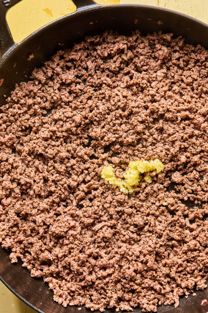 Cooked ground beef with minced garlic in a skillet.