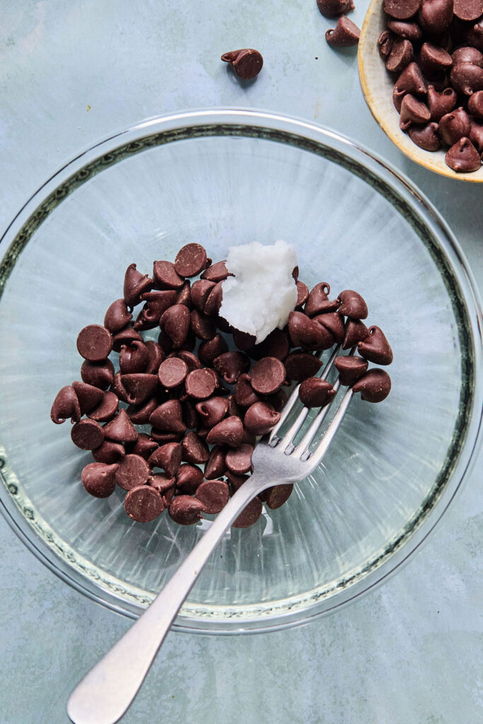 Chocolate chips and coconut oil in a bowl with a fork.