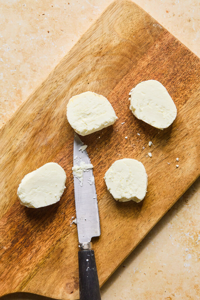 Sliced of goat cheese on a cutting board with a knife.