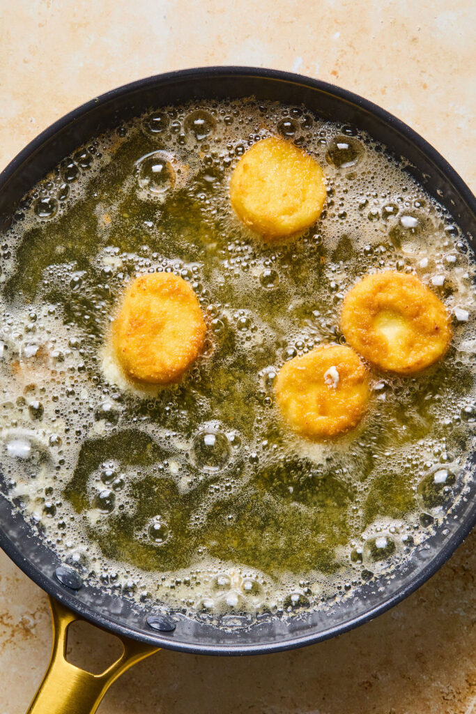Goat cheese slices frying in oil in a skillet.