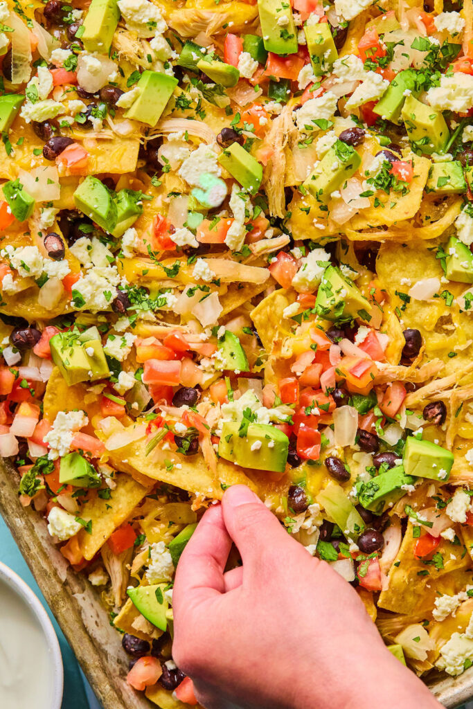 Chicken sheet pan nachos with a hand holding a tortilla chip.