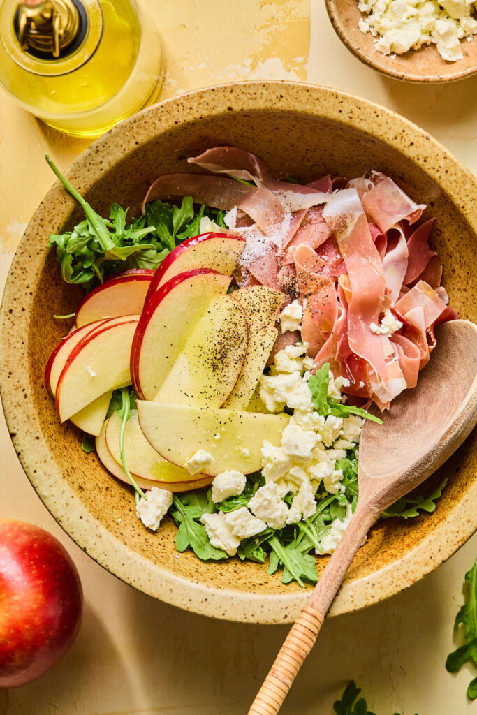 Ingredients for Proscuitto Apple Arugula Salad in a bowl before being mixed together.