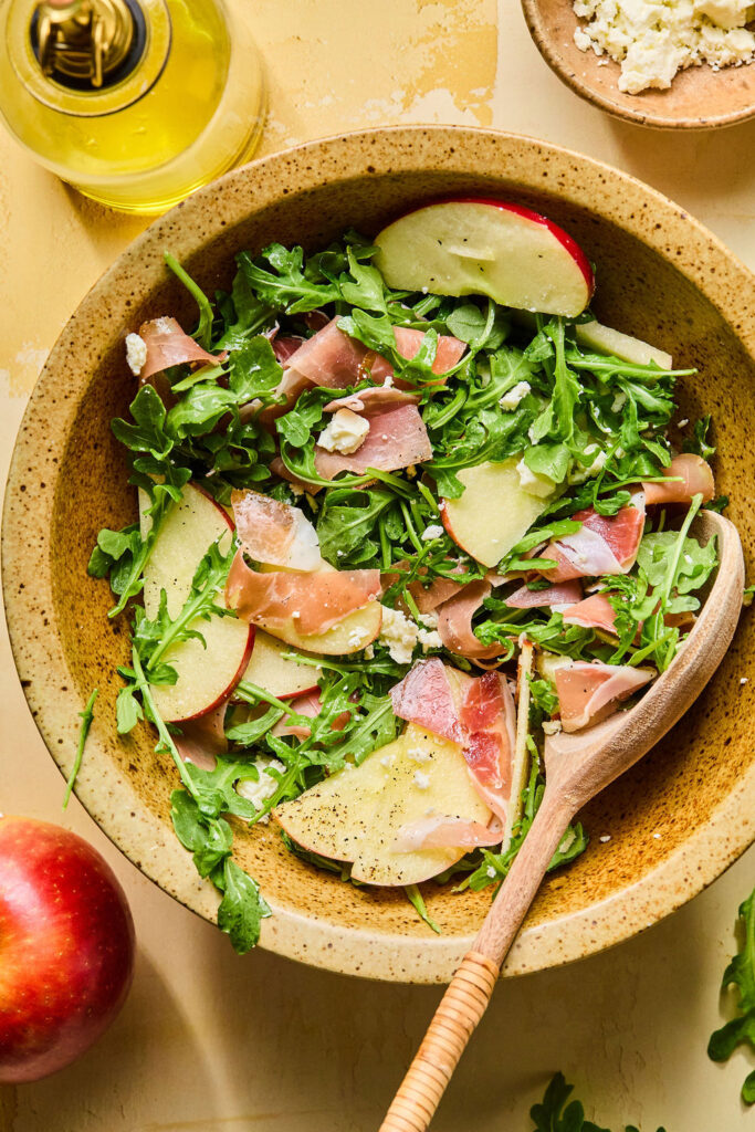 Proscuitto Apple Arugula Salad ingredients being tossed together.