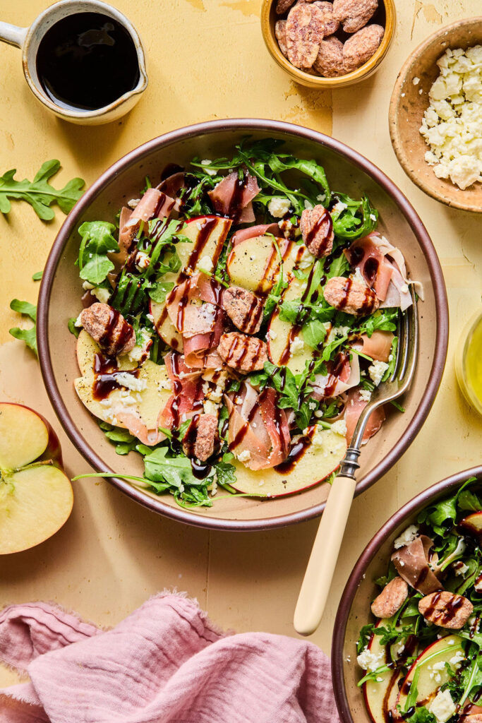 Proscuitto Apple Arugula Salad in a bowl drizzled with balsamic glaze.