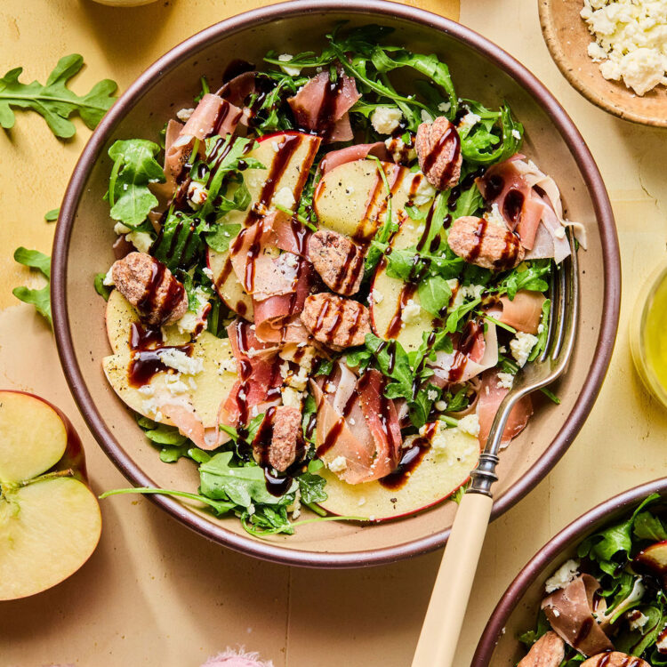 Proscuitto Apple Arugula Salad in a bowl drizzled with balsamic glaze.