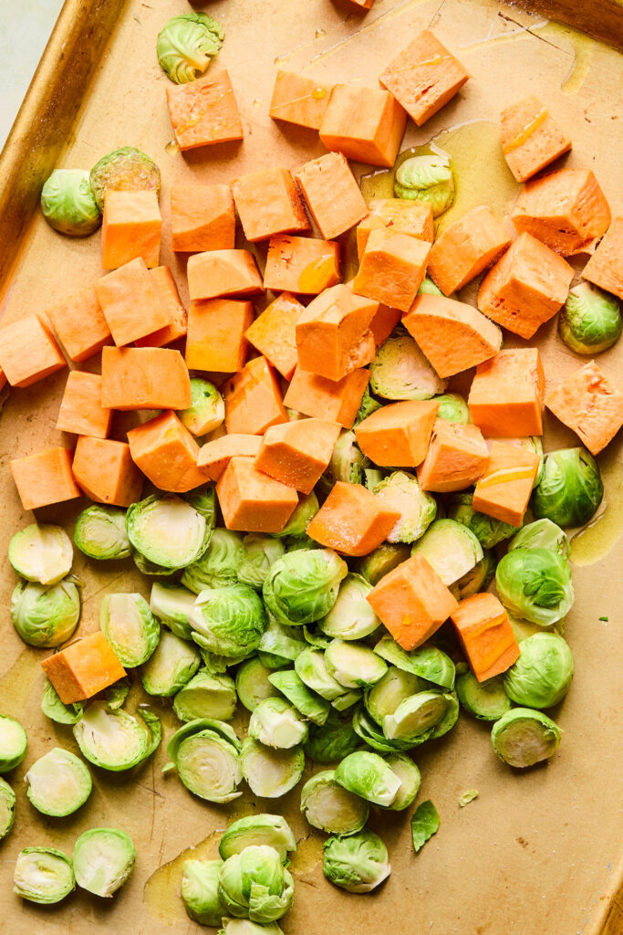 Cut up sweet potatoes and brussels sprouts on a sheet pan.