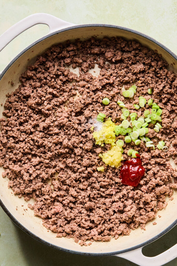 Ginger, garlic, and onions beign added to the cooked gorund beef in a skillet.