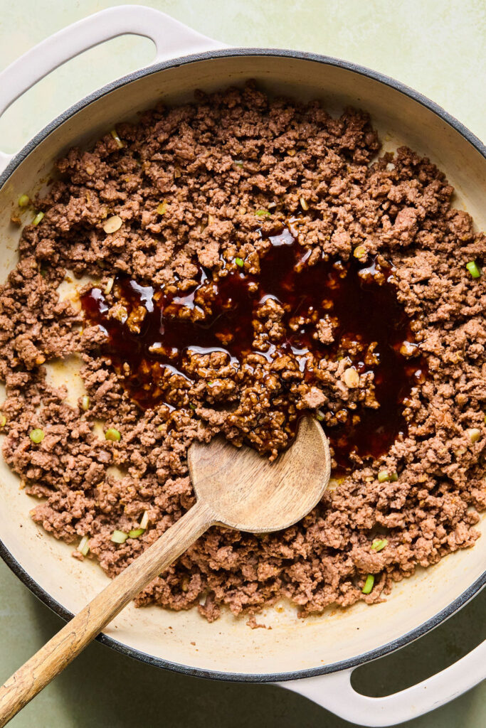 Korean BBQ sauce being added to the ground beef in the skillet.
