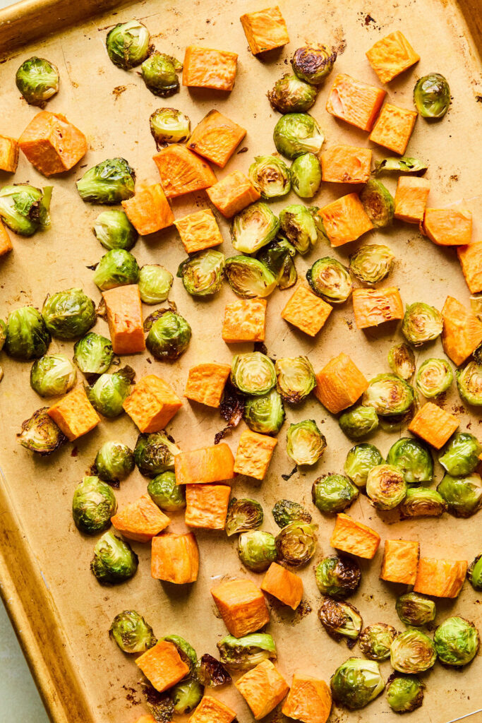 Cut up sweet potatoes and brussels sprouts on a sheet plan after being roasted.