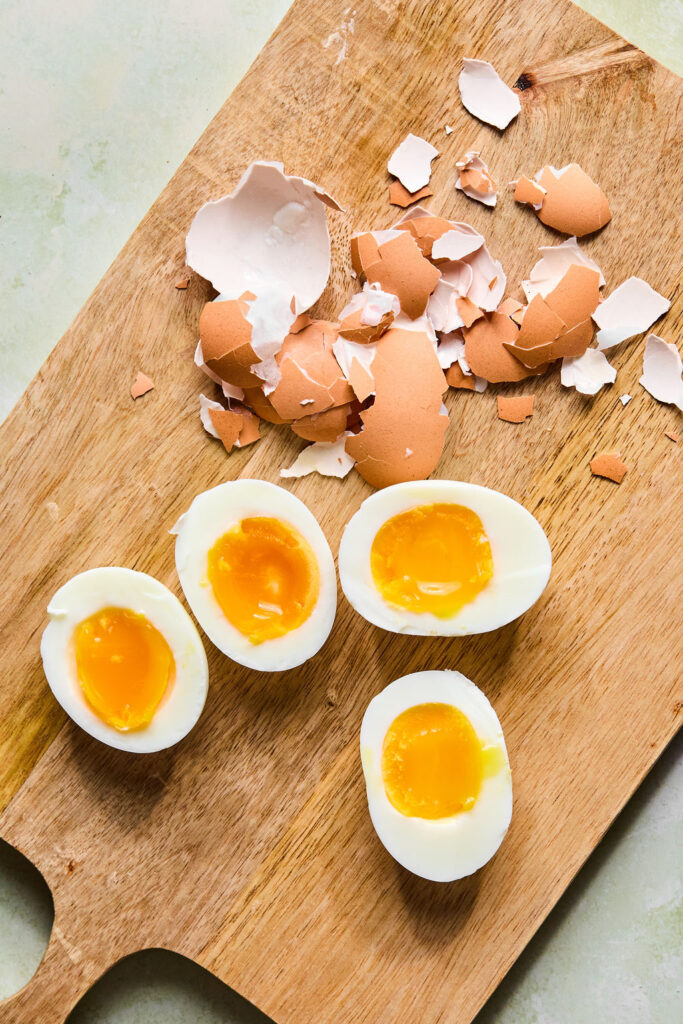 Hardboiled eggs being peeled on a cutting board.