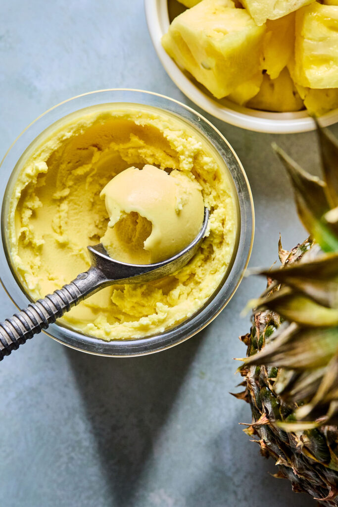 Ninja Creami Pineapple Sorbet in a Ninja creami pint with an ice cream scoop.