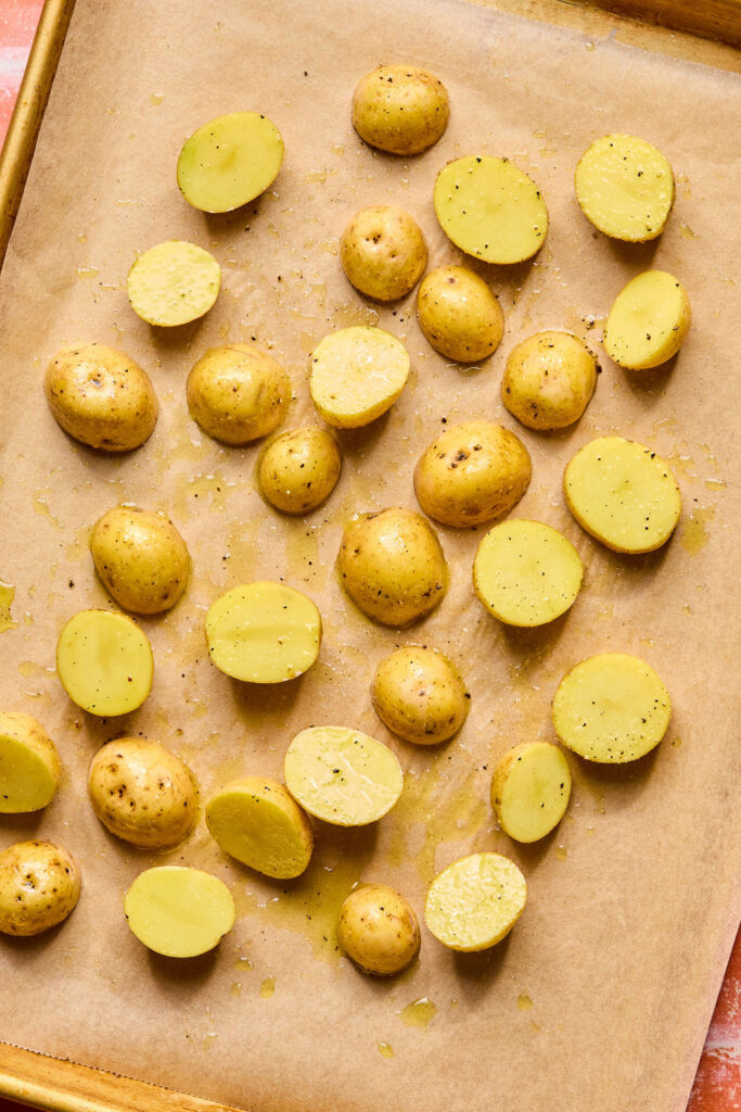 Baby potatoes cut in half on a baking sheet.