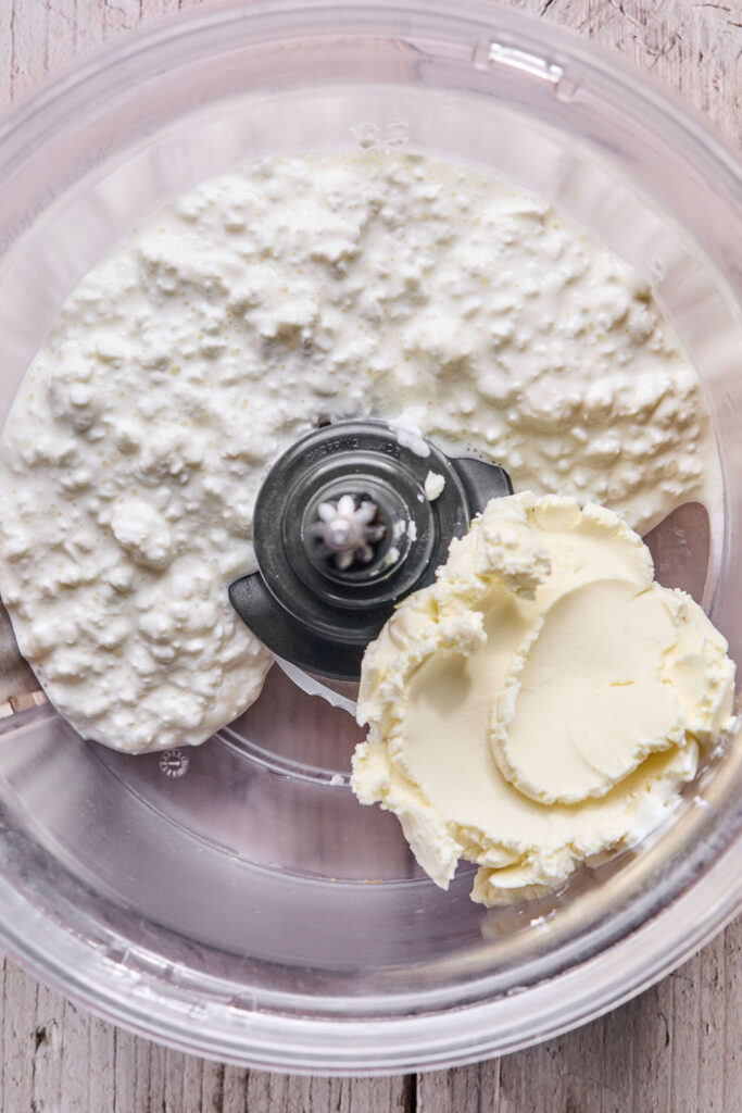 Cottage cheese and cream cheese in a food processor bowl before being combined.