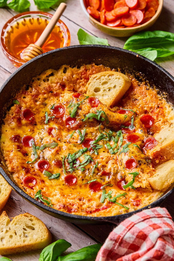 Hot Honey Pizza Dip with small slices of bread being dipped in it.