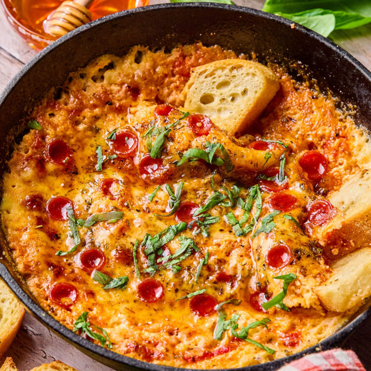 Hot Honey Pizza Dip with small slices of bread being dipped in it.