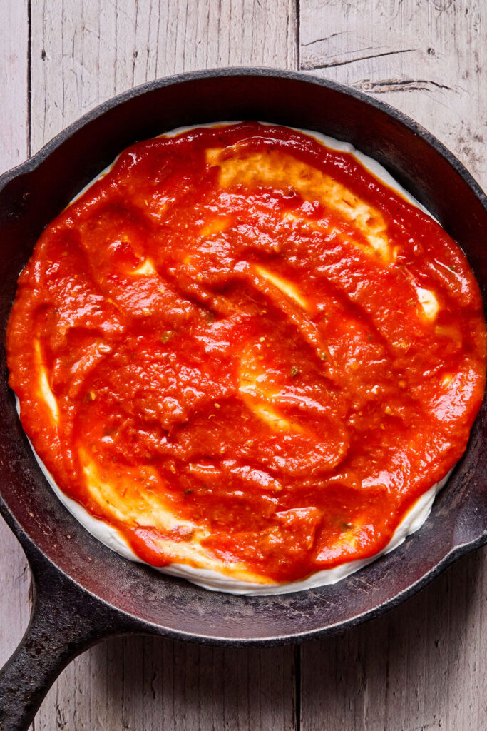 Marinara sauce on top of the cheese mixture in a round dish.