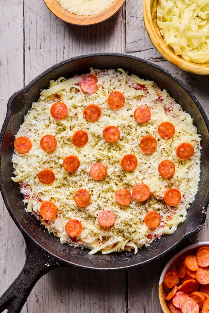 Shredded cheese and pepperoni on top of the marinara sauce.