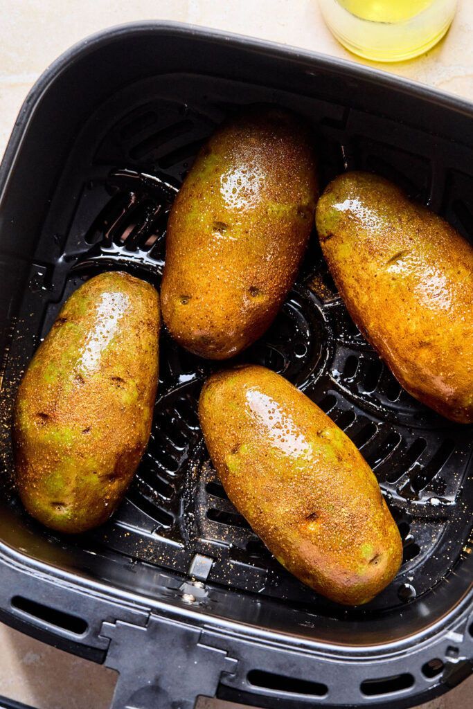 Halved potaoes face down in an air fryer basket.