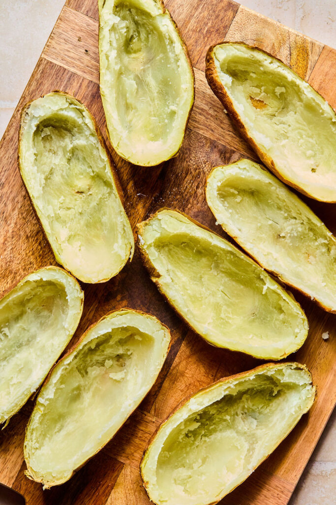 Halved potatoes with some of the inside scooped out on a cutting board.