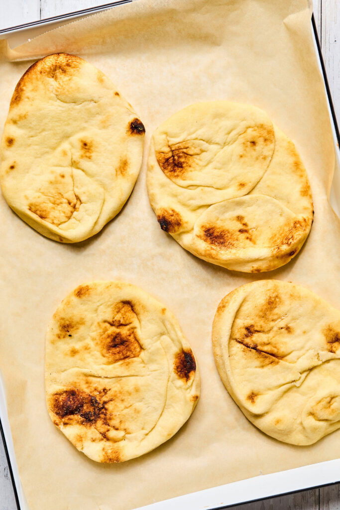 Naan bread on a sheet pan with parchment paper.