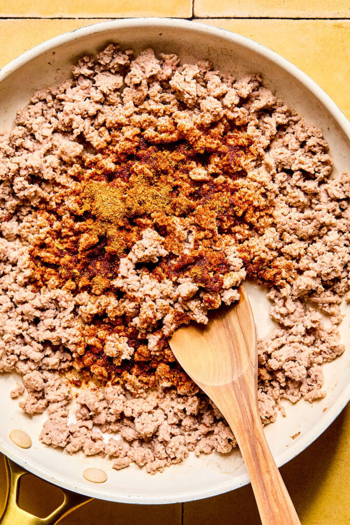 Cooked ground turkey topped with seasonings in a skillet.