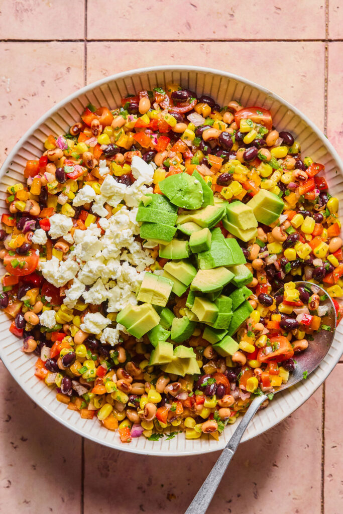 Rainbow Cowboy Caviar topped with feta cheese and avocado in a large bowl.
