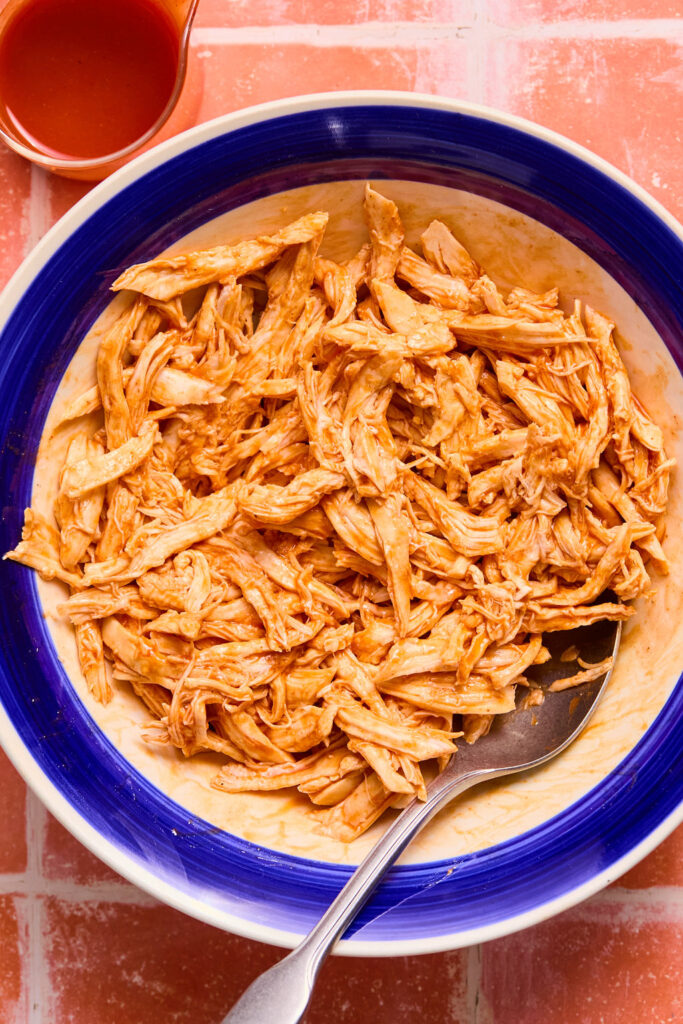Shredded chicken with buffalo sauce in a small with a spoon.