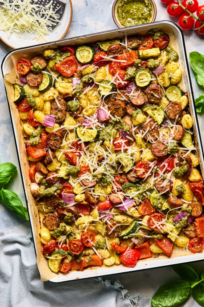 Sheet Pan Chicken Sausage & Veggie Gnocchi topped with shredded cheese on a baking sheet.