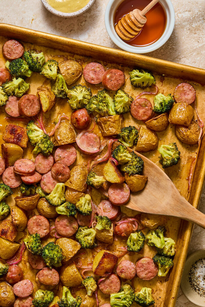 Honey Mustard Chicken Sausage and Potato Sheet Pan on a baking sheet with a wooden spoon.