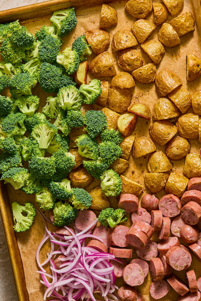 Chicken sausage, broccoli, and red onion on a baking sheet.
